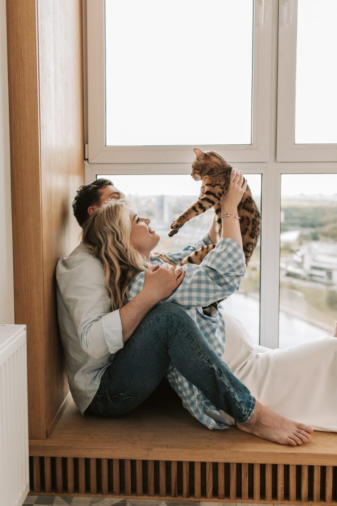 Un couple joue avec son chat près d’une fenêtre